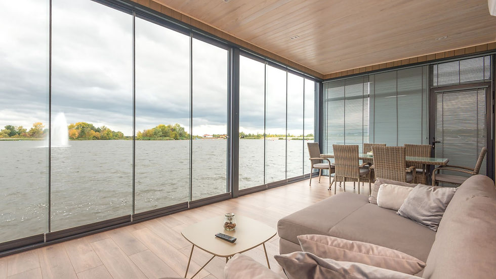 Interior of spacious modern villa with comfortable sofa and glass walls overlooking wavy lake under cloudy sky