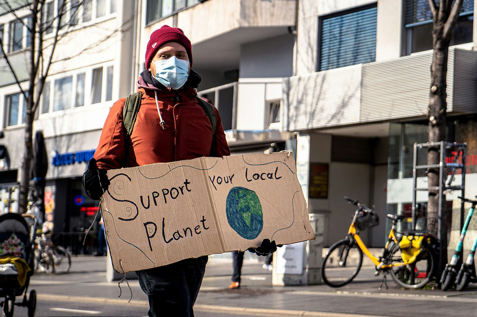 A person walking holding a cardboard sign that says "Support Your Local Planet" with a drawing of planet Earth.