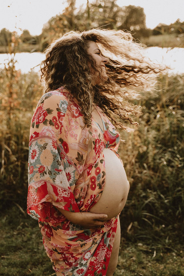Pregnant woman in floral dress outdoors, hair flowing in the wind, editorial maternity photography