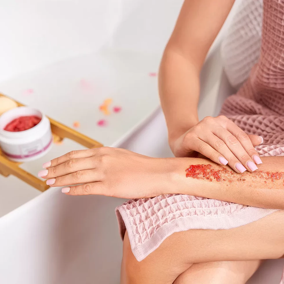 Mulher aplica esfoliante vermelho no braço, tratamento de spa