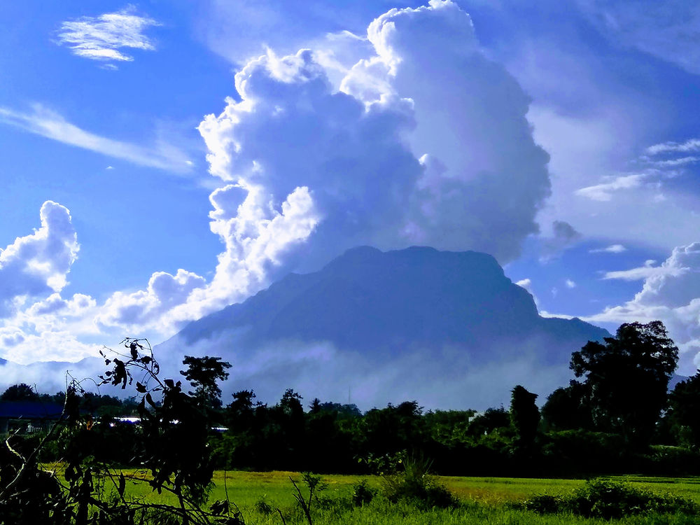 Massive white clouds towering over a mist-covered mountain