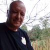 Jean Claude Grimaldi smiling outdoors with trees behind him
