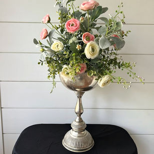 A large silver-plated vase featuring a tall base attached containing a floral arrangement.