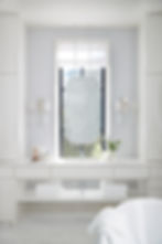 Minimalist bathroom with a central frosted mirror, white vanity, towels, vase with flowers, and natural light from a window, evoking calm.