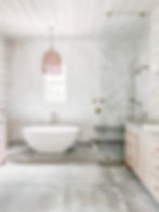 Modern bathroom with freestanding tub, glass shower, wood cabinets, and a woven pendant light. Bright, airy atmosphere with grey tiles.