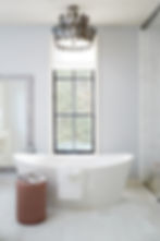 Luxurious bathroom with a white freestanding tub, towel, and open magazine. Elegant chandelier, black window, and beige stool add style.