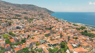 Vista aérea da cidade do Funchal, Madeira, com o crescimento urbano e empresarial da baía, ilustrando os desafios jurídicos da expansão de empresas na Região