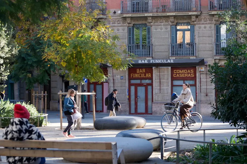 Pedestrians and a cyclist in a Superilla public space in the Eixample, Barcelona, with a traditional neighbourhood bar in the background
