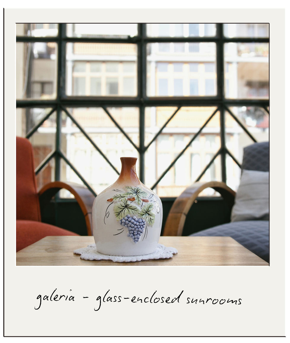 Ceramic vase with floral design on a wooden table in a sunroom with large windows. Text reads "galeria - glass-enclosed sunrooms."