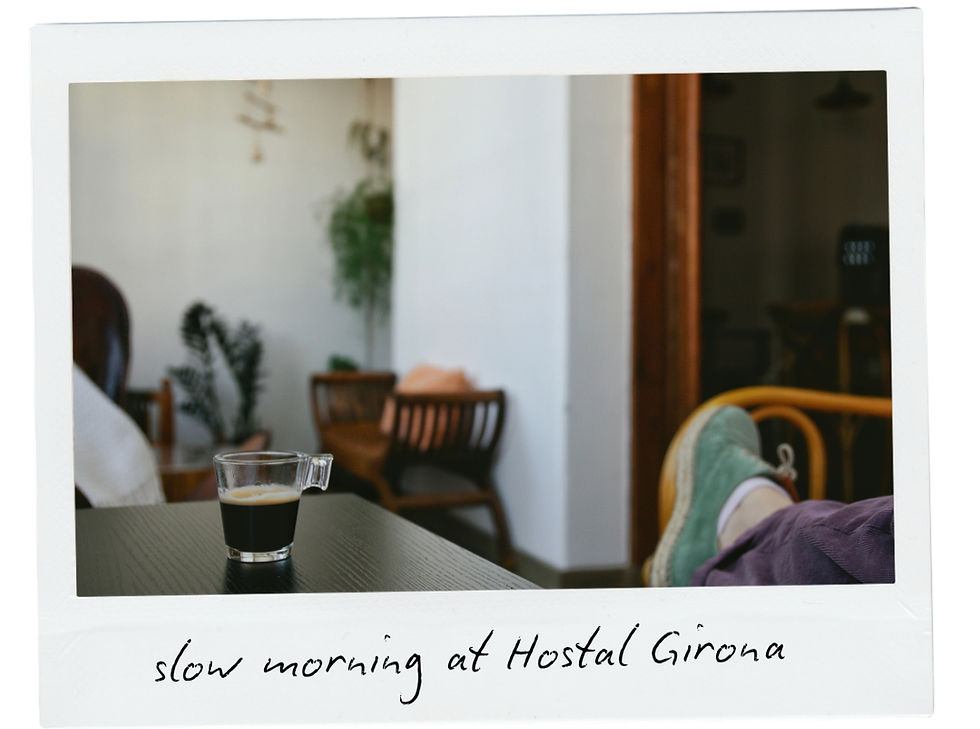 Cozy scene at Hostal Girona. A person relaxes with feet up, sipping coffee. Indoor plants and wooden chairs in the background. Calm mood.
