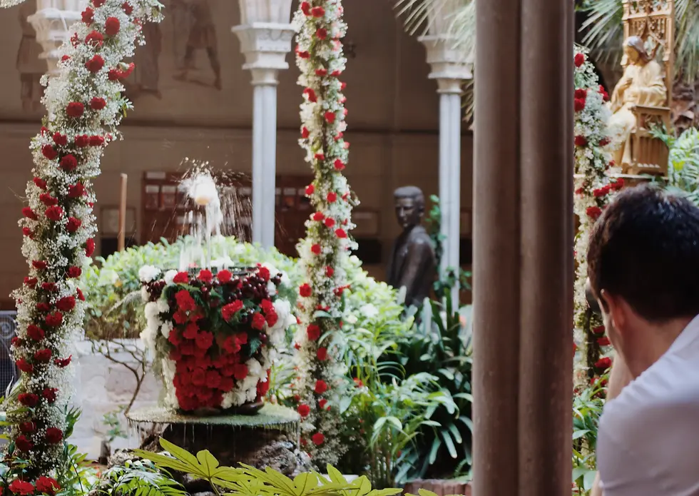 Decorated courtyard in Barcelona with floral arches and the traditional L’Ou com Balla fountain during Corpus Christi, a Catalan festival celebrating creativity and heritage.