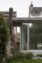 Extension moderne en béton et verre d'une maison traditionnelle en briques, intégrant une grande baie vitrée avec vue sur le jardin. Conception contemporaine créant un contraste élégant entre l'ancien et le moderne, offrant un espace intérieur lumineux et en harmonie avec la nature.