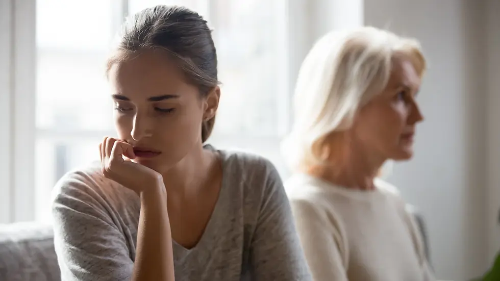 Two women sit back-to-back indoors, one younger with a pensive expression, the other older looking away, representing the emotional gap in parent-child estrangement.