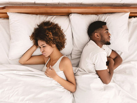 couple sitting apart on a bed looking disapointed and disconnected, illustrating intimacy challenges and mismatched sexual desire in a relationship.