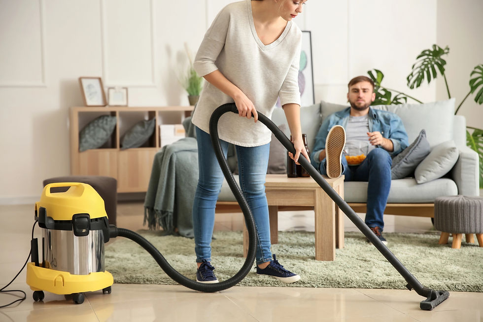 Woman vacuuming while her partner sits on the couch eating. Reflecting overfunctioning in a relationship