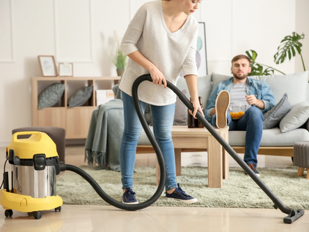 Woman vacuuming while her partner sits on the couch eating. Reflecting overfunctioning in a relationship