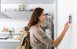 Lady activating the intruder alarm from the touchscreen control panel in her kitchen