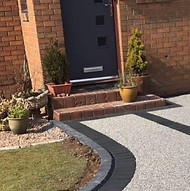 A modern brick house entrance with a dark door, potted plants on each step