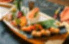 Sushi and sashimi boat featuring salmon, shrimp, ebi prawn, tuna and sushi rolls, with vibrant greens and orange in the elegant main dining room