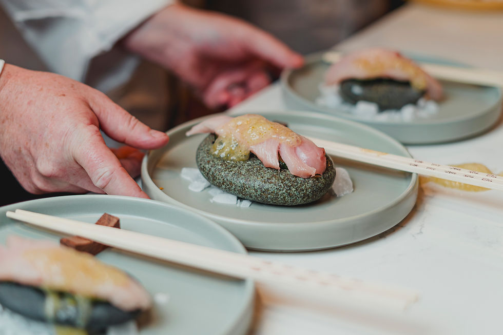 Chef arranging nigiri-style bites on stones over ice