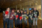 Group holding roses and lanterns, smiling at the camera, inside a building.