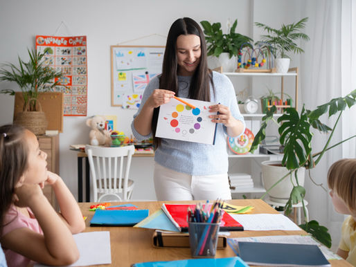 A teacher holding a color chart and instructing young students in a classroom, representing a multiple subject teaching credential and hands-on learning in an elementary education setting