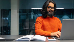 An adult professional working on a laptop in a modern office, representing a masters degree organizational leadership and advanced leadership development through online learning