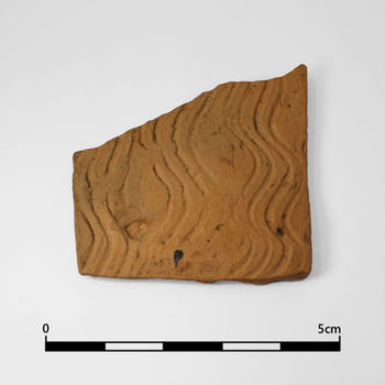 Brownish orange Ceramic Building Material (CBM) shard with wavy incised patterns on its surface, shown next to a 5cm scale for size reference.