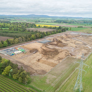 A drone overhead shot of the entire archaeological excavation, visible as a large area of open earth amongst green fields and woodland.