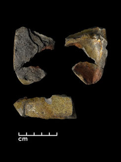 A small, broken, triangular-shaped shallow ceramic dish. It is mostly covered in a shiny green glaze, although the bottom is grey, where the glaze has come off. It is shown from the top, bottom, and side, with a black background.