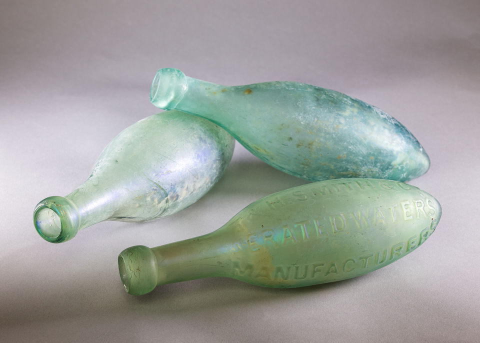 Three blue-green bottles lay flat, with one leaning on top of another. They are oval in shape, with a slightly pointed bottom and a standard oval mouth.