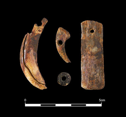 Three pieces of yellowish-brown bone, all with small drill holes, and a small black round ceramic bead sit on a black background.