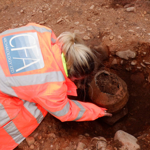 An archaeologist excavates an urned cremation.