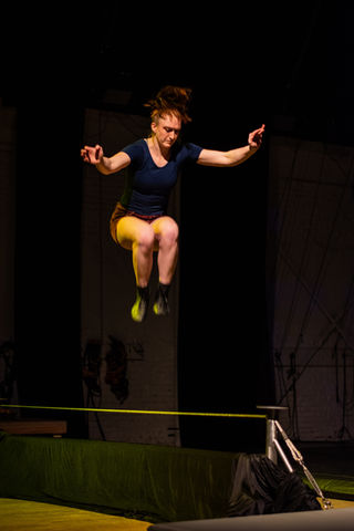 Meghan McClure jumps into the air from a tightwire, with her arms stretched out to the sides 