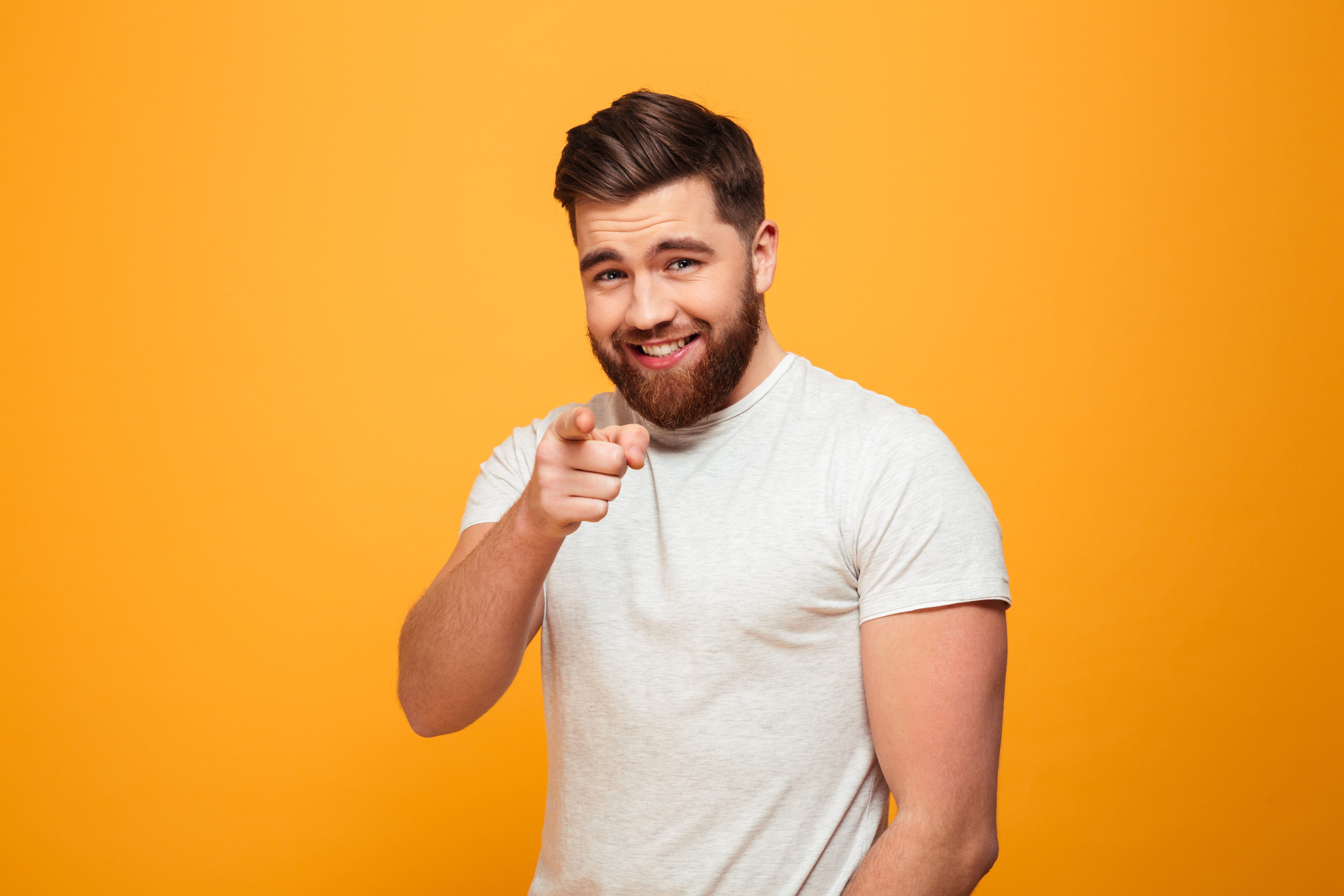 Portrait of a smiling bearded man pointing finger at camera isolated over yellow backgroun