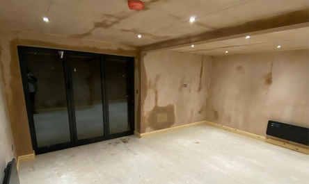 An unfinished garage conversion with exposed walls and ceiling, construction in progress, featuring recessed lighting and large sliding doors.
