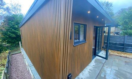 Modern wooden-clad garden office, a garage conversion masterpiece, with sliding doors and exterior lighting.