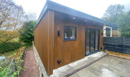 A modern garage conversion outhouse with wooden cladding and sliding glass doors.