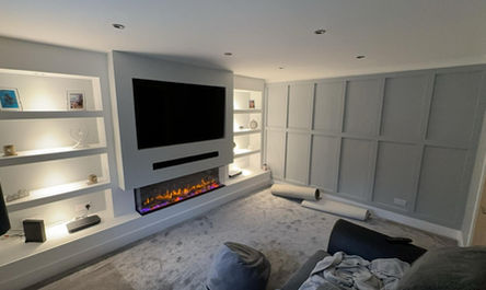 Garage conversion before and after: Modern living room with wall-mounted TV above an electric fireplace, surrounded by built-in shelving.
