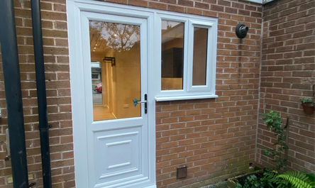 A white door and a window on a brick house facade with a garage conversion in Crewe, including a paved pathway leading up to the entrance.