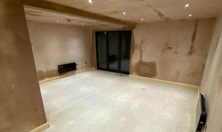 A garage conversion before and after: an unfurnished room undergoing renovation with exposed wiring and plastered walls.