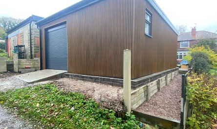 A modern, standalone structure showcasing a modern shed with a roller shutter door and a corrugated metal facade, situated adjacent to a residential building.
