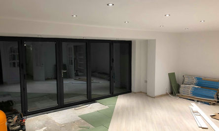 Interior under construction for a garage conversion in Urmston with sliding doors, recessed lighting, and construction materials on the floor.