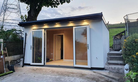 Modern small garden house with sliding doors and exterior lighting at dusk, featuring a garage conversion.