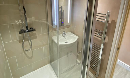 Modern bathroom, a result of a garage conversion before and after, featuring a glass shower enclosure, wall-mounted sink, and heated towel rack.
