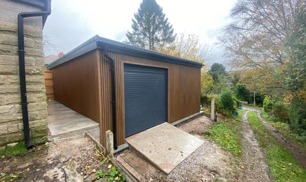 A contemporary brown garden shed converted into a garage with a roller shutter door at the side of a residential property.