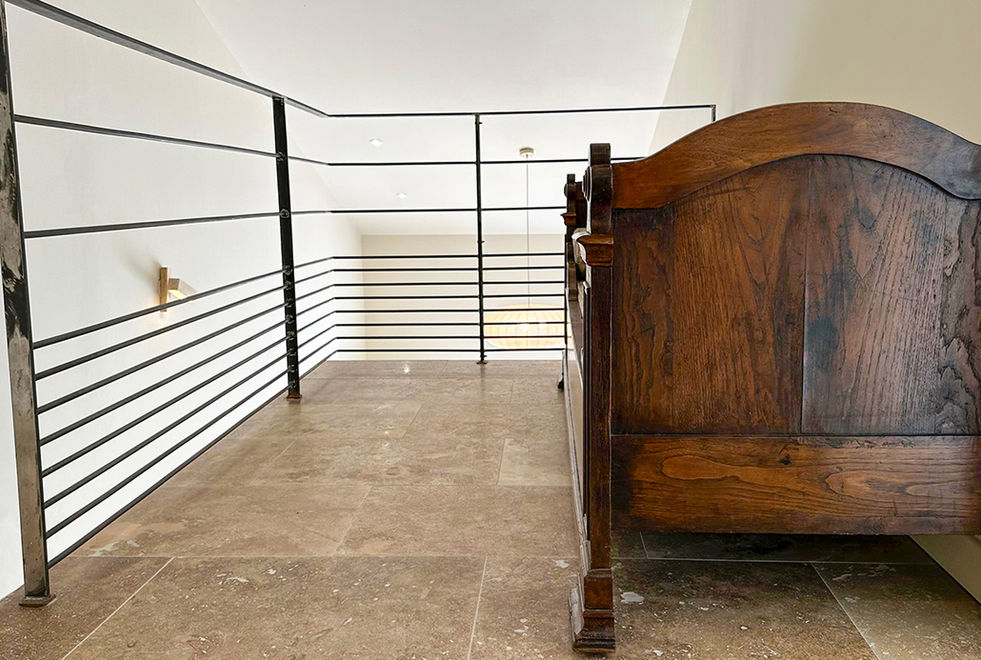 Palier mezzanine avec tête de lit en bois ancien, garde-corps en fer forgé noir et sol en travertin, villa Corse Solenzara