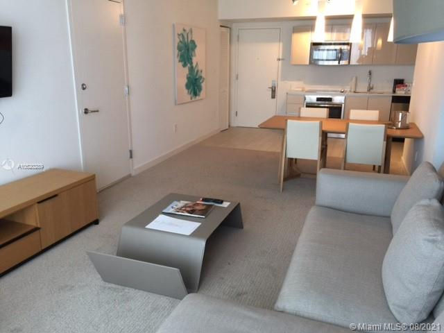 View of open-plan living room and kitchen in a short-term rental condo featuring worn carpet, soon to be upgraded with waterproof luxury vinyl flooring by Not Just Carpet for enhanced durability and appeal