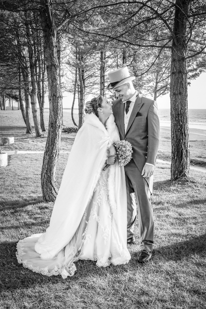 bride and groom laugh as they pose for a photo on Swansea bay