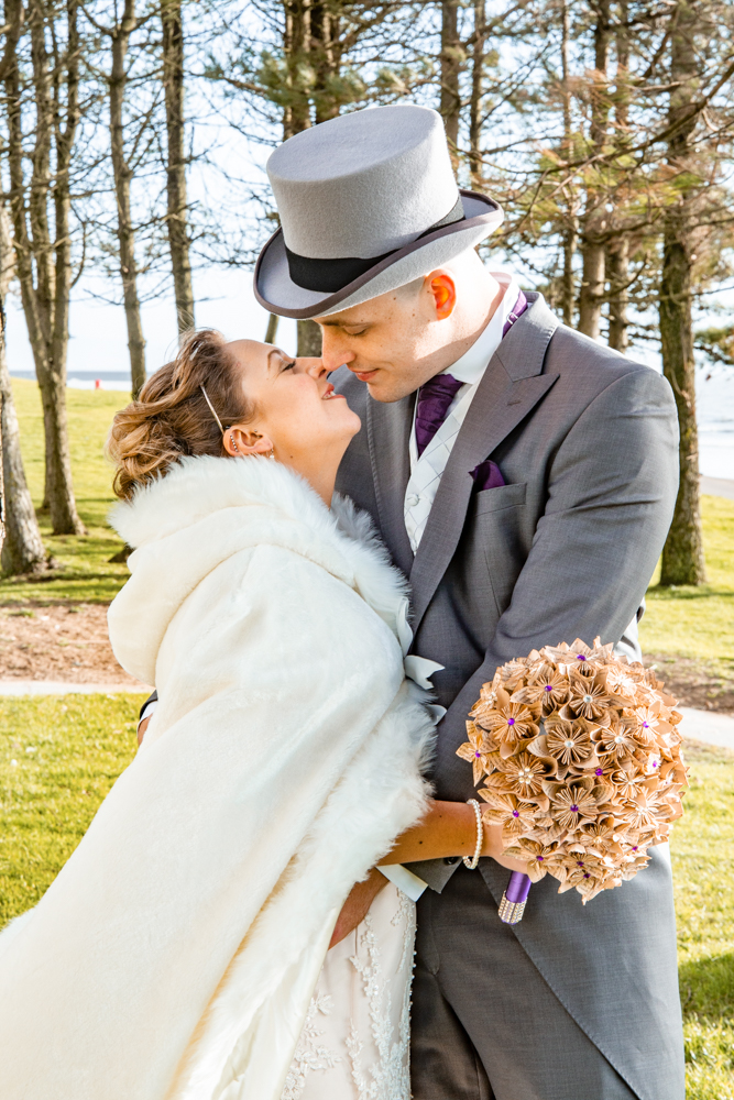 bride and groom stand for a photo on Swansea bay